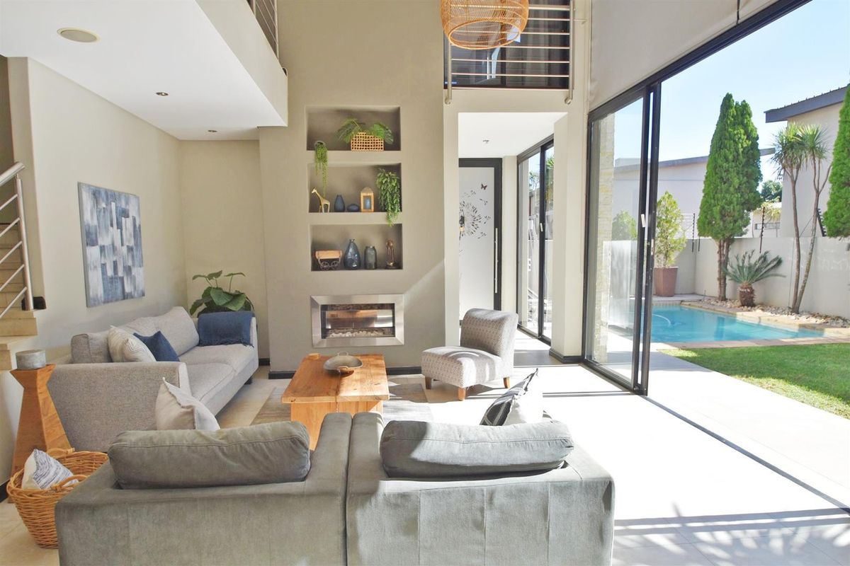 Spacious living room with high ceilings, built-in fireplace, recessed shelving, and large sliding glass doors opening to a private pool and garden area.