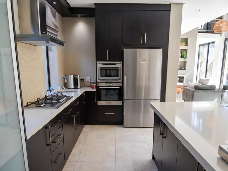 Modern kitchen featuring dark wood cabinetry, stone countertops, integrated stainless steel appliances, gas hob, and recessed lighting, flowing into an open-plan living area.