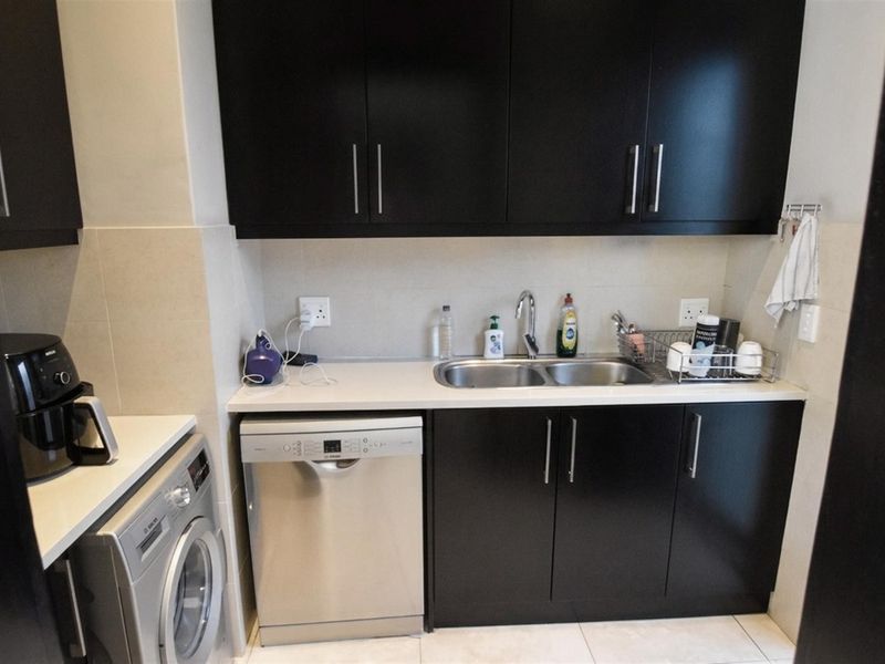 A functional scullery featuring dark cabinetry, a double bowl sink, tiled splashback, and dedicated space for a dishwasher and washing machine.