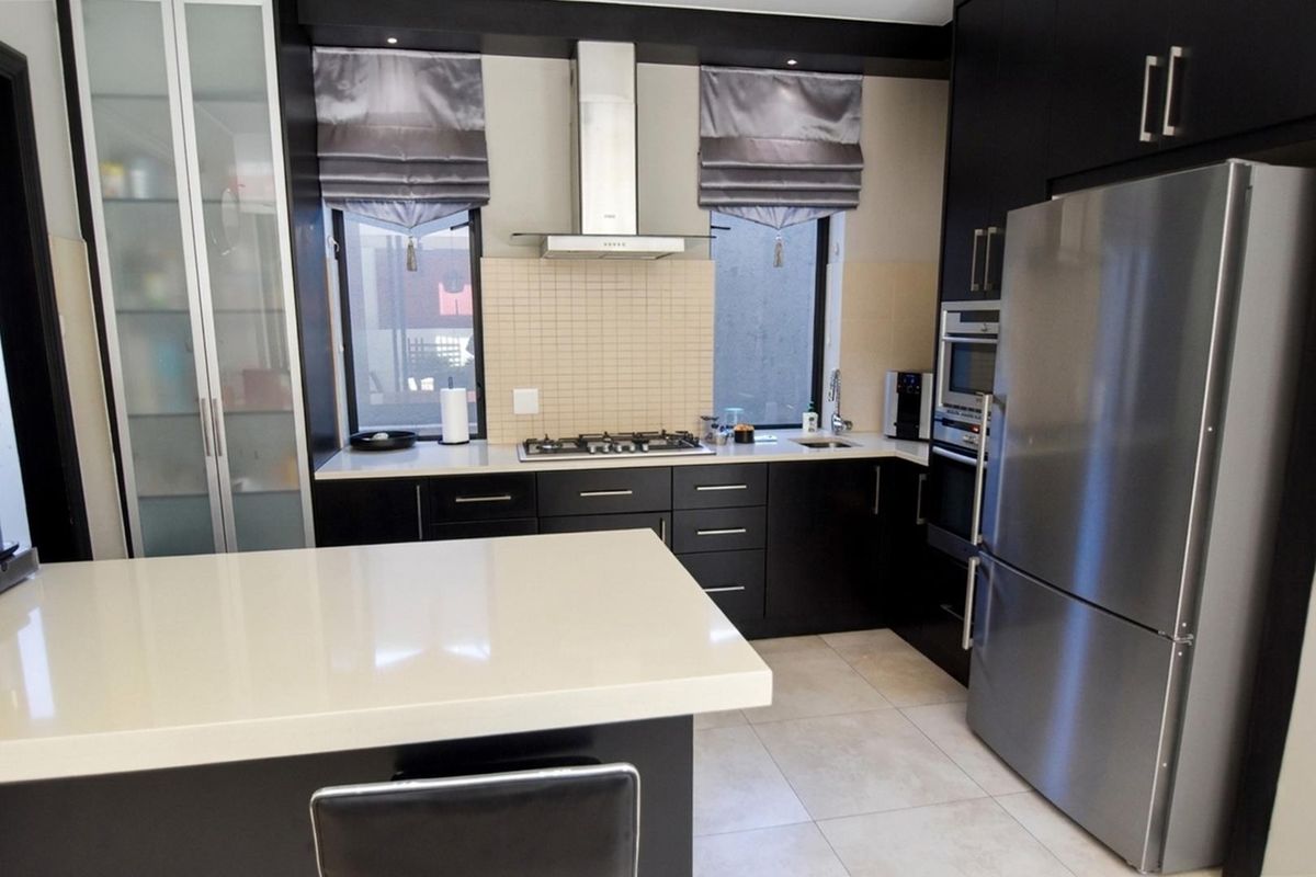 Modern kitchen featuring dark cabinetry, quartz countertops, gas hob, stainless steel extractor fan, and integrated appliances with a clean, contemporary finish.