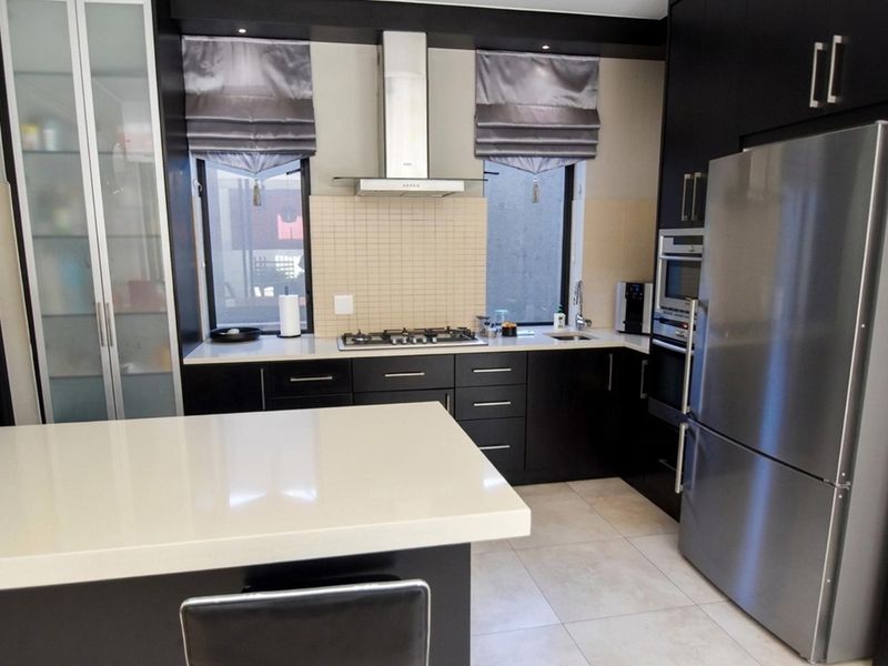 Modern kitchen featuring dark cabinetry, quartz countertops, gas hob, stainless steel extractor fan, and integrated appliances with a clean, contemporary finish.