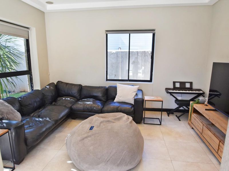 A bright living room featuring neutral tiled flooring, large sliding windows, and recessed ceiling lighting, providing a clean and functional space.