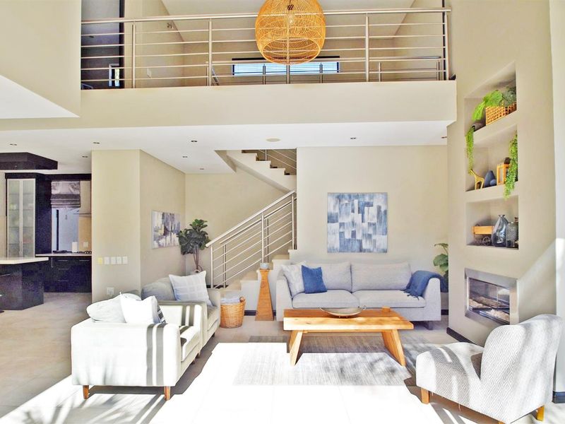 Spacious open-plan living area featuring a double-volume ceiling, built-in fireplace, recessed shelving, and a mezzanine level overlooking the lounge.