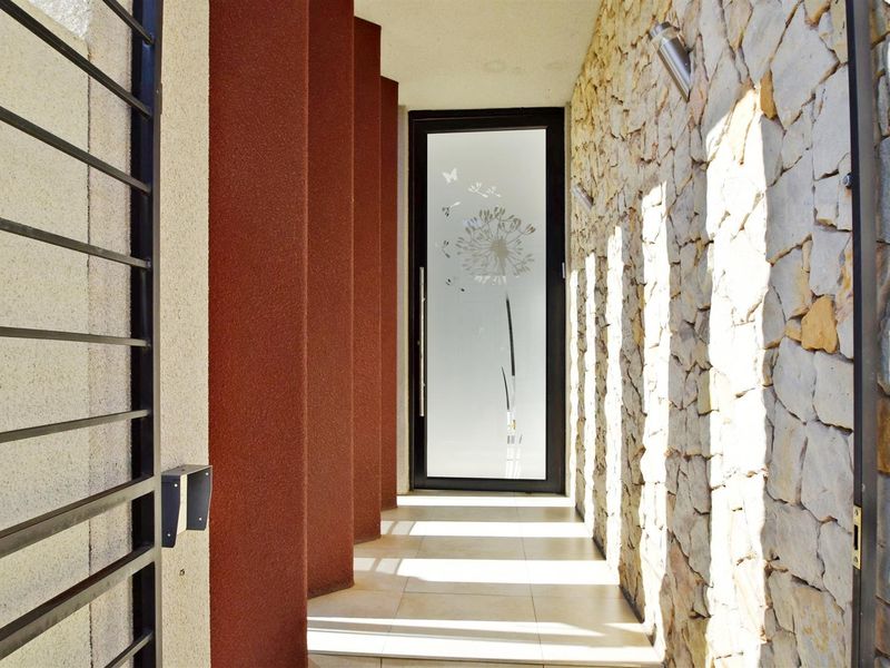 A modern entrance walkway featuring natural stone cladding, tiled flooring, and a decorative glass front door with architectural lighting.
