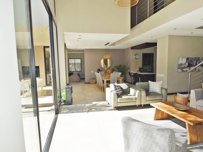 Spacious open-plan living and dining area featuring double-volume ceilings, large sliding doors for natural light, and a modern staircase with metal balustrades.