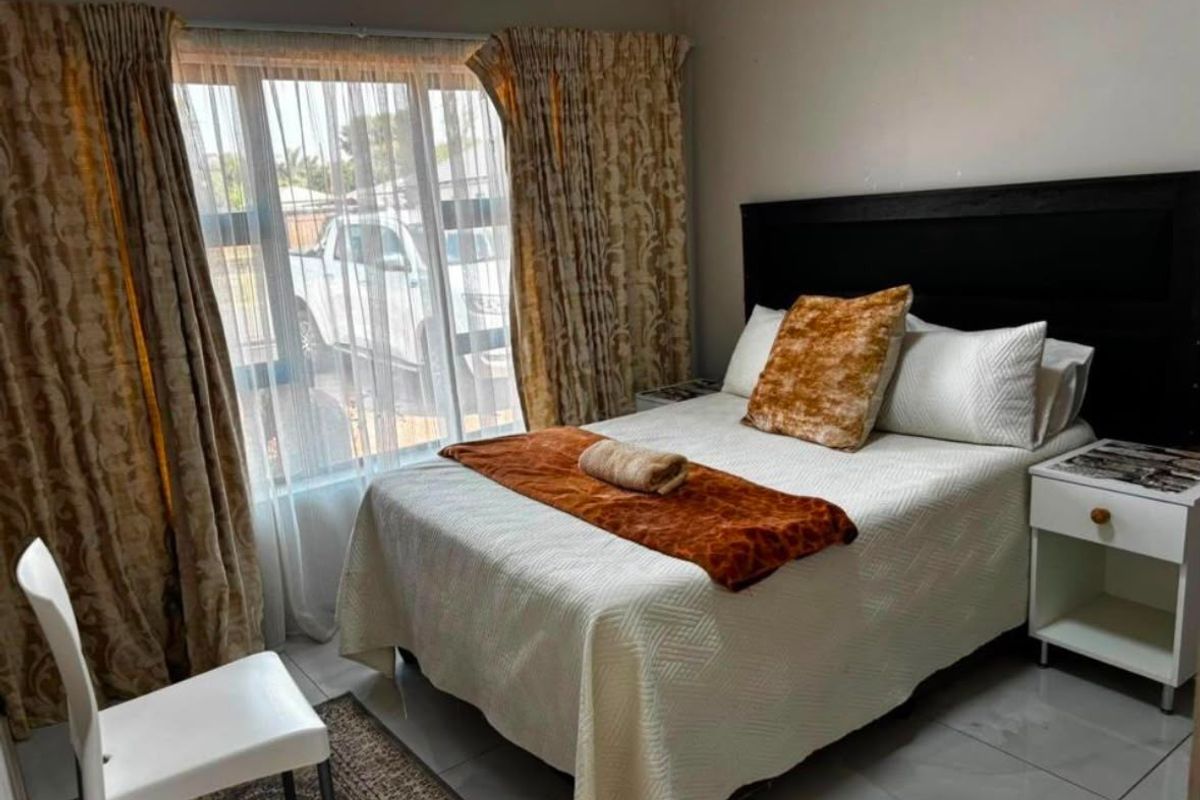 A functional bedroom featuring tiled flooring and large windows with curtain rails, providing natural light and a comfortable living space.