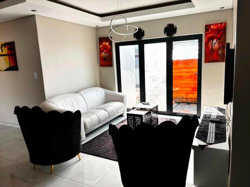 Modern living room featuring tiled flooring, a recessed ceiling design, and black aluminium sliding doors providing access to the outdoor area.