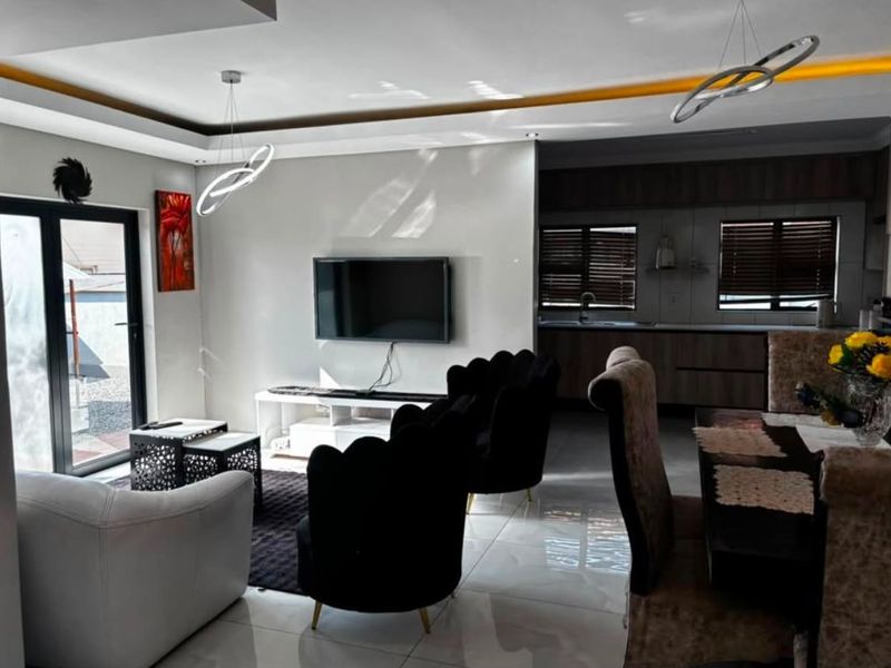 Modern open-plan living and dining area featuring sleek tiled floors, recessed ceiling lighting, and a seamless transition to a contemporary kitchen space.