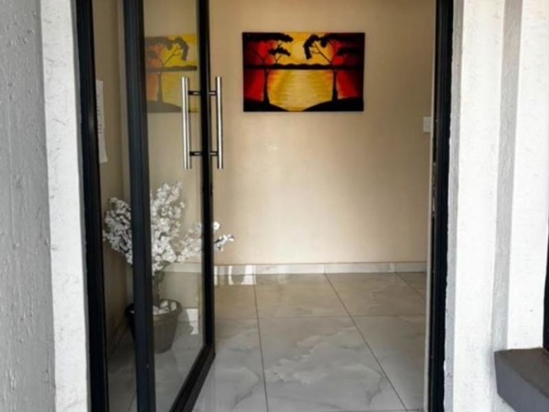 A bright entrance hall featuring modern tiled flooring and a contemporary black aluminium frame glass door.