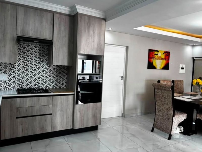 Modern open-plan kitchen and dining area featuring contemporary wood-grain cabinetry, integrated appliances, patterned tile backsplash, and polished floor tiles.