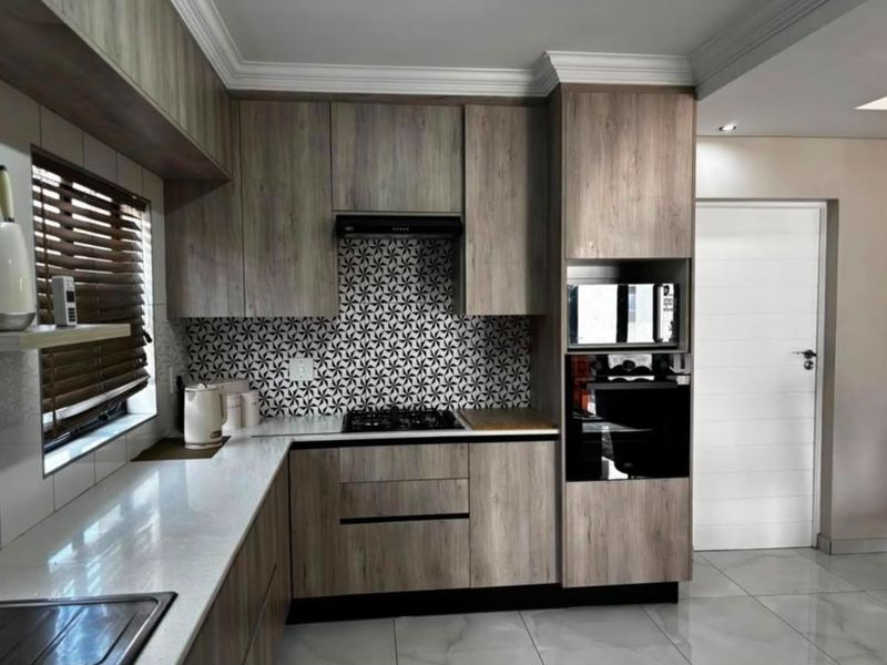 Modern kitchen featuring wood-grain cabinetry, stone countertops, built-in appliances, and a striking patterned tile backsplash.
