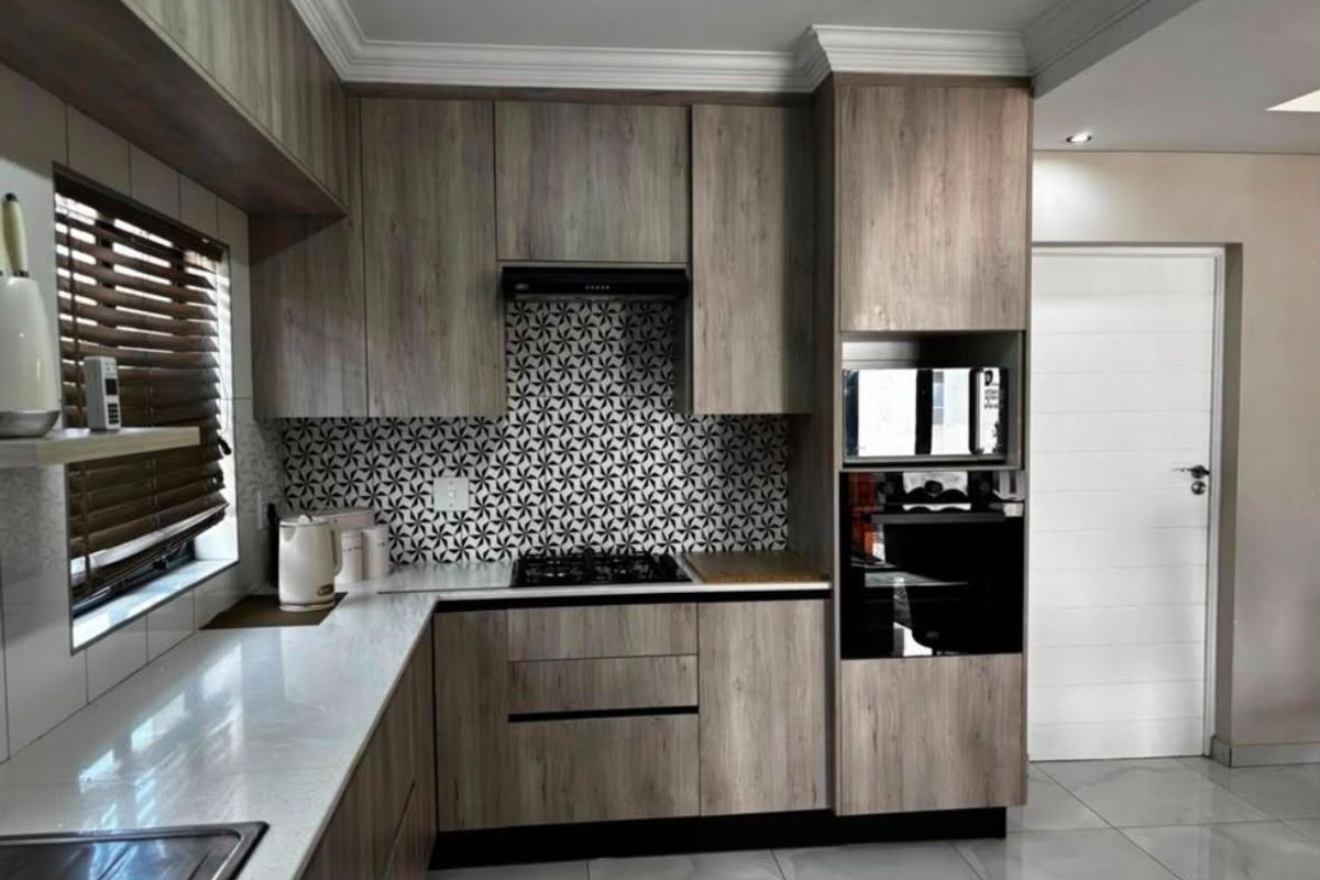 Modern kitchen featuring wood-grain cabinetry, stone countertops, built-in appliances, and a striking patterned tile backsplash.