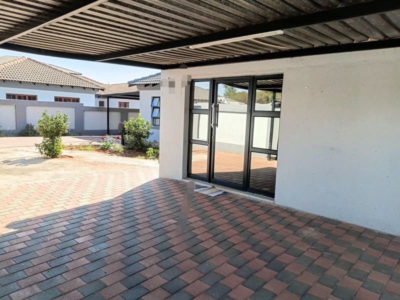 A covered outdoor patio area featuring paved flooring and a modern black aluminium frame glass door leading into the home.