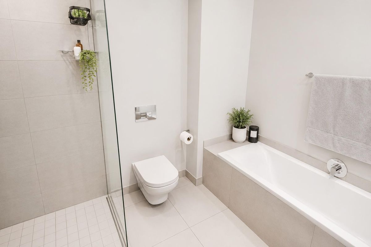 Modern bathroom featuring a wall-hung toilet with concealed cistern, a glass-enclosed shower, and a built-in bathtub with neutral tiled finishes.
