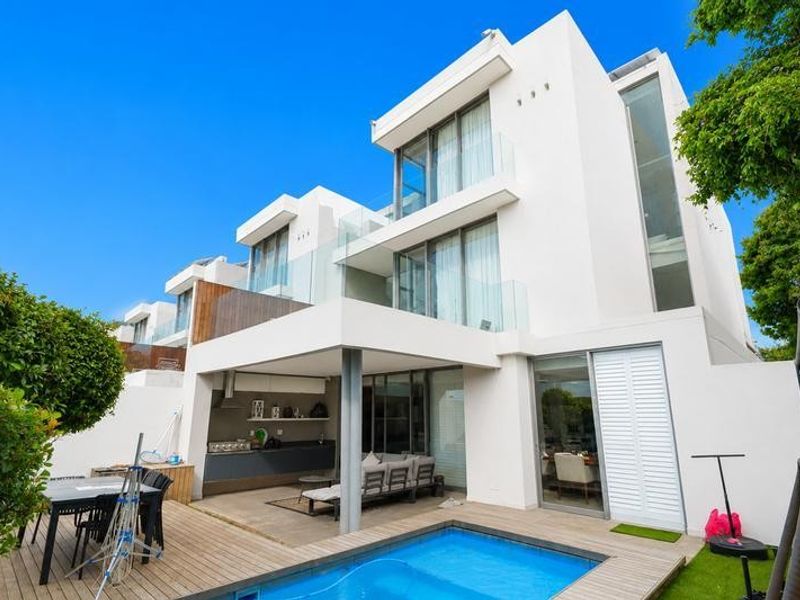 Modern townhouse rear elevation featuring a swimming pool, timber deck, covered patio with built-in braai, and multi-level glass-fronted balconies.