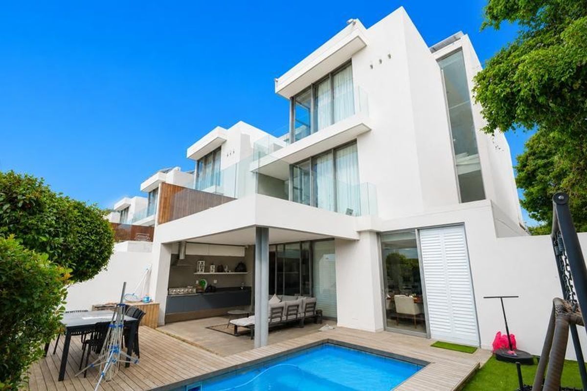 Modern townhouse rear elevation featuring a swimming pool, timber deck, covered patio with built-in braai, and multi-level glass-fronted balconies.