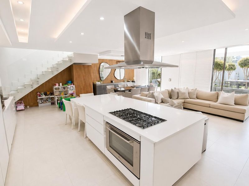 Modern open-plan living area featuring a sleek kitchen island with integrated appliances, timber feature wall, and a contemporary floating staircase with glass balustrade.