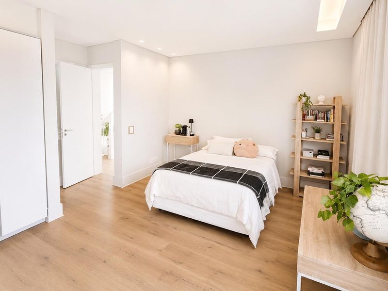 A bright and modern bedroom featuring light wood-look laminate flooring, built-in wardrobe storage, and recessed ceiling lighting.