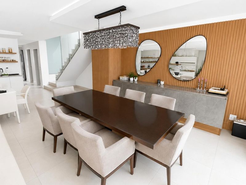 Modern dining area featuring elegant slatted timber wall paneling, built-in cabinetry, and a sleek staircase with a glass balustrade.
