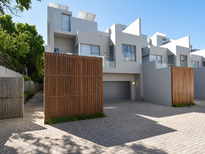 Modern townhouse exterior featuring a paved driveway, automated garage, timber privacy screening, and contemporary architectural design with glass balcony balustrades.