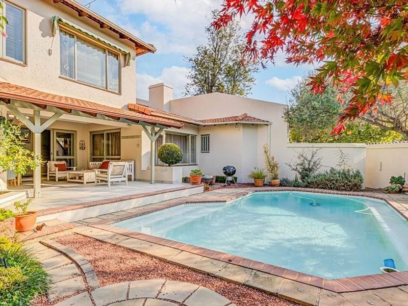 A well-maintained rear garden featuring a swimming pool, paved surround, and a covered patio area attached to the main house structure.