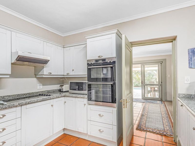 A well-maintained kitchen featuring white shaker-style cabinetry, granite countertops, a built-in double oven, and terracotta floor tiles, with direct access to the patio.