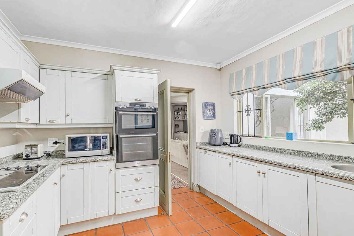 A well-maintained kitchen featuring white shaker-style cabinetry, granite countertops, built-in appliances, and terracotta floor tiles, offering a functional and classic workspace.