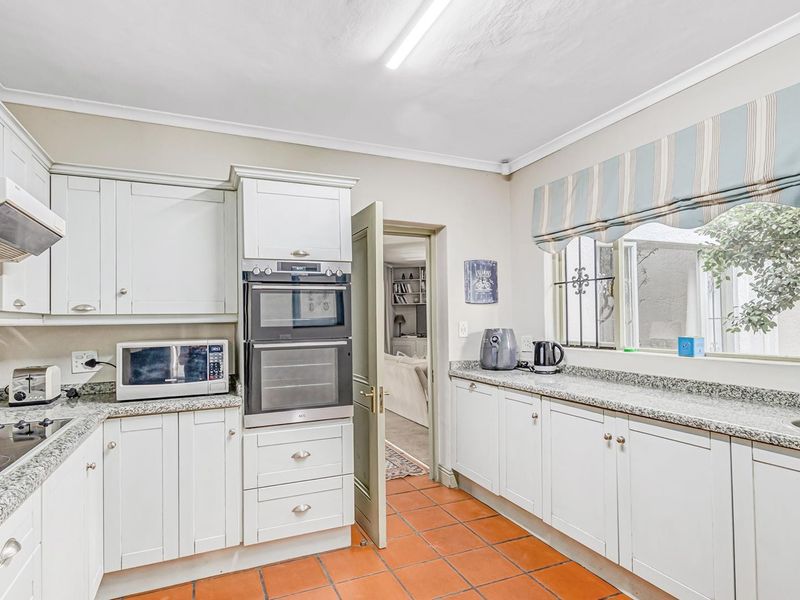 A well-maintained kitchen featuring white shaker-style cabinetry, granite countertops, built-in appliances, and terracotta floor tiles, offering a functional and classic workspace.