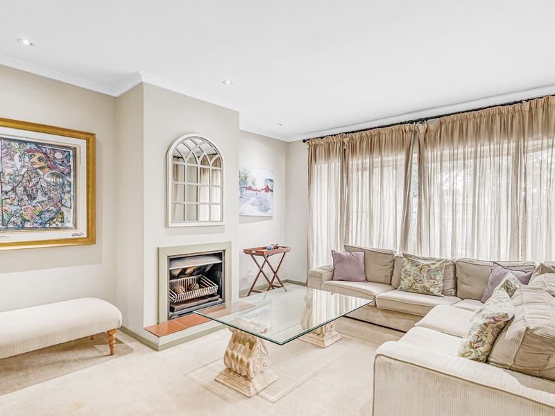 A bright and comfortable living room featuring a built-in fireplace, recessed downlighting, and large windows with floor-to-ceiling curtains.