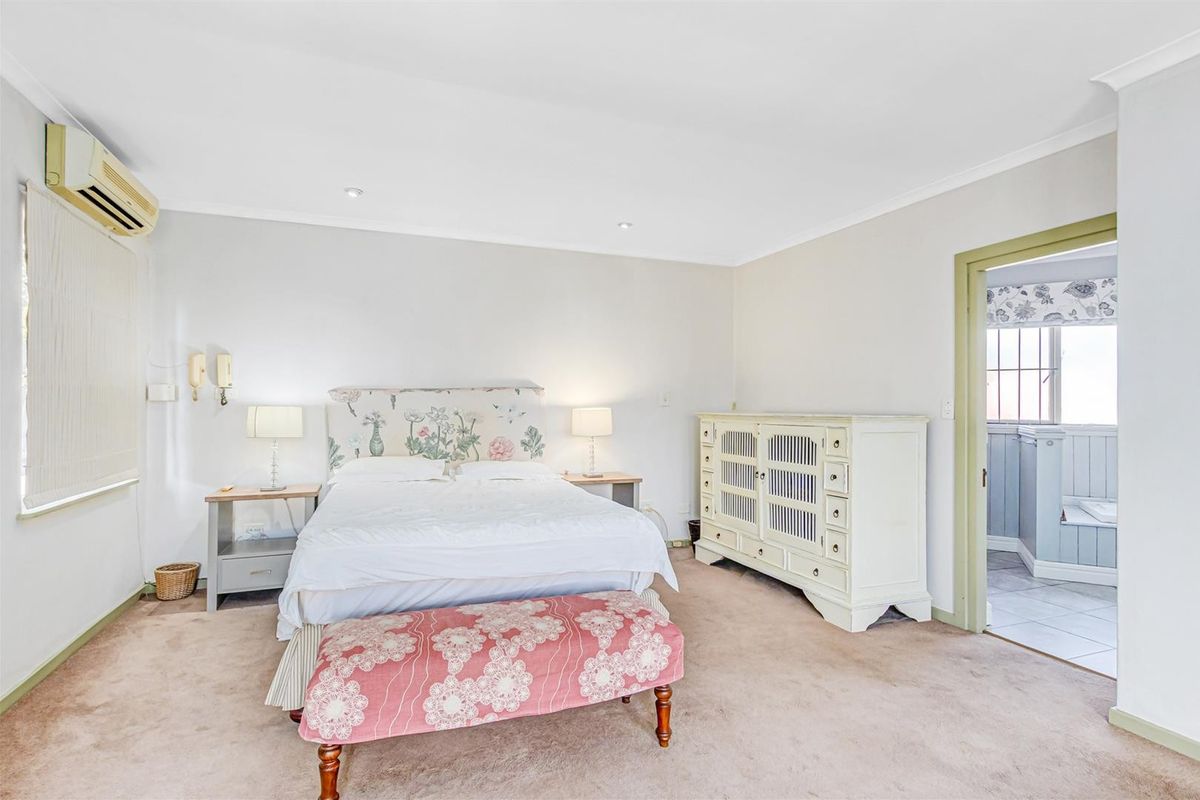 Spacious bedroom featuring neutral walls, carpet flooring, recessed downlighting, and a wall-mounted split-system air conditioner, with an adjoining ensuite bathroom.