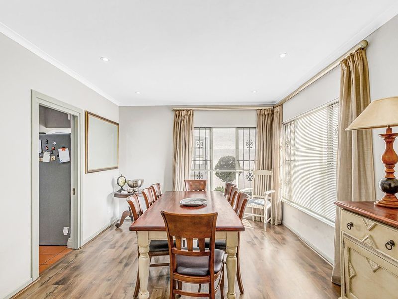 A well-lit dining room featuring laminate flooring, recessed downlighting, and large windows with fitted blinds and curtain tracks.