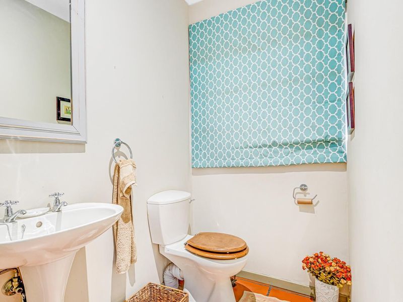 A compact guest bathroom featuring a pedestal sink, standard toilet, and wall-mounted mirror with neutral wall finishes.