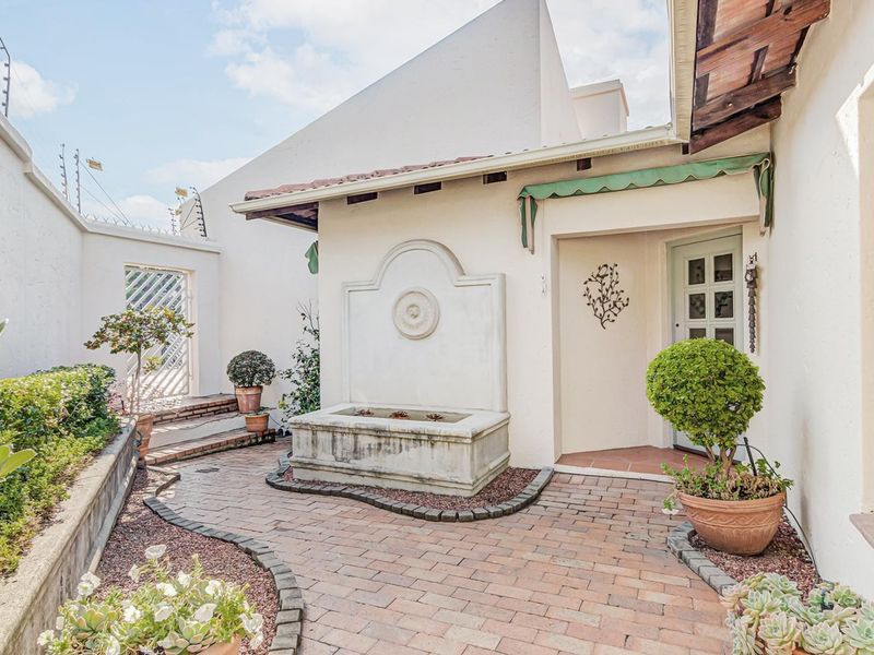 A charming front entrance courtyard featuring brick paving, a decorative stone water feature, and secure perimeter walling with electric fencing.