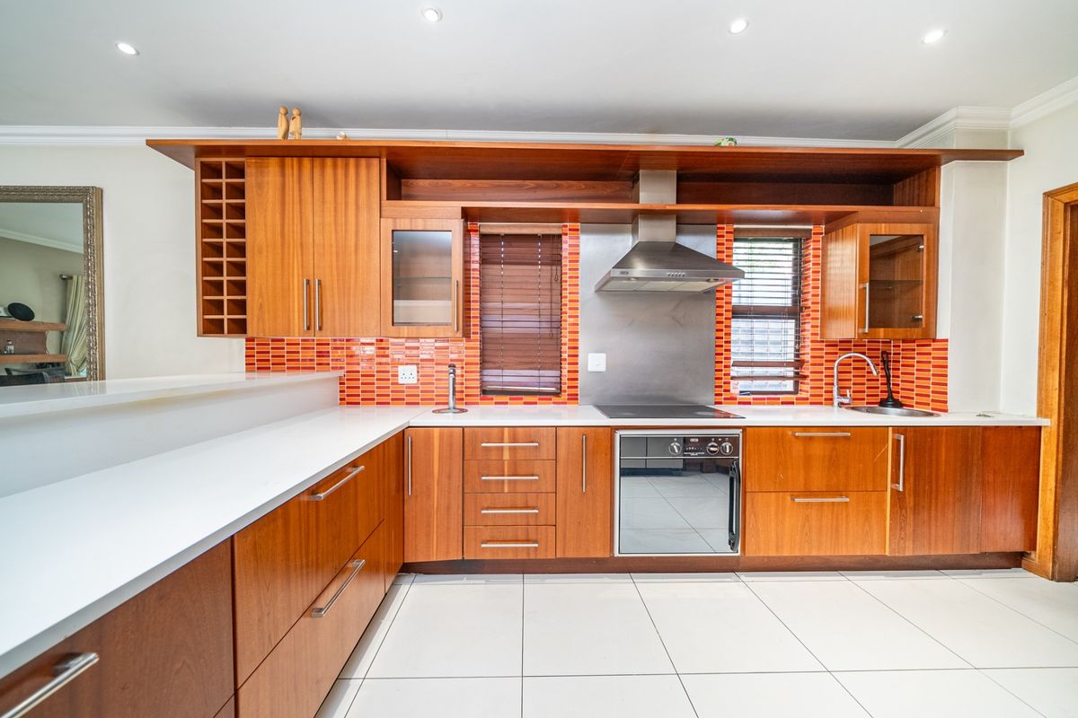A well-maintained kitchen featuring warm wooden cabinetry, stone countertops, a built-in oven with extractor fan, and a vibrant tiled splashback.
