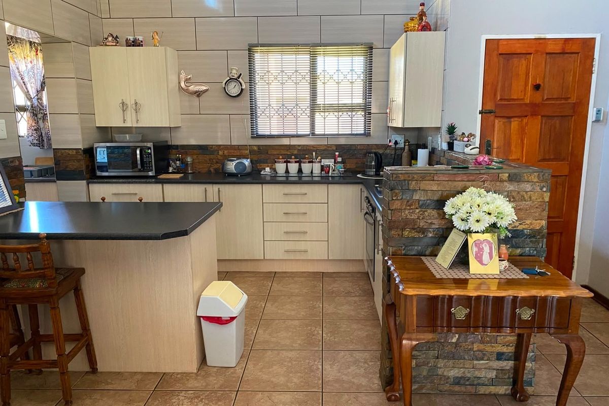 A functional kitchen featuring light-toned cabinetry, stone-cladding accents, tiled flooring, and a breakfast bar, providing a practical layout for daily meal preparation.
