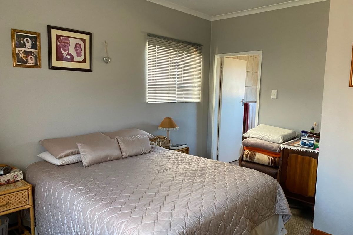 A functional bedroom featuring neutral wall tones, carpeted flooring, and a window fitted with venetian blinds, providing access to an adjoining bathroom.