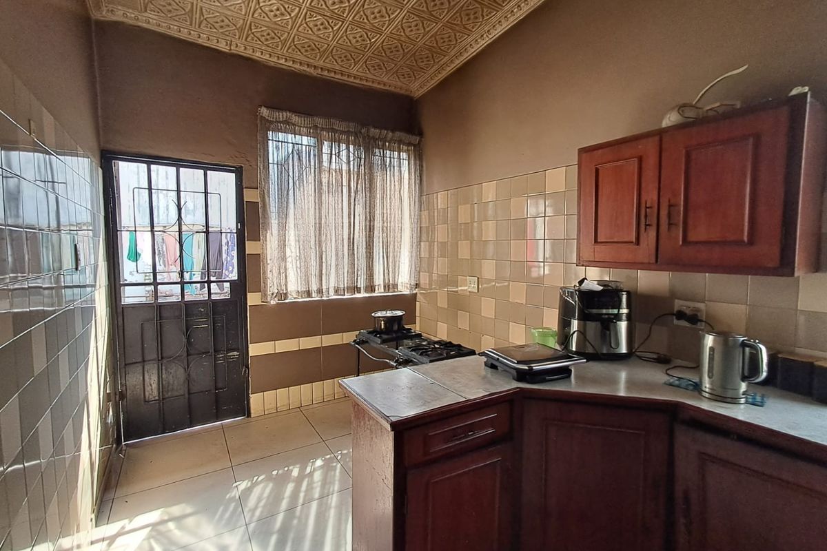 A functional kitchen featuring built-in wooden cabinetry, tiled splashbacks, and a decorative ceiling, with direct access to the exterior via a security gate.