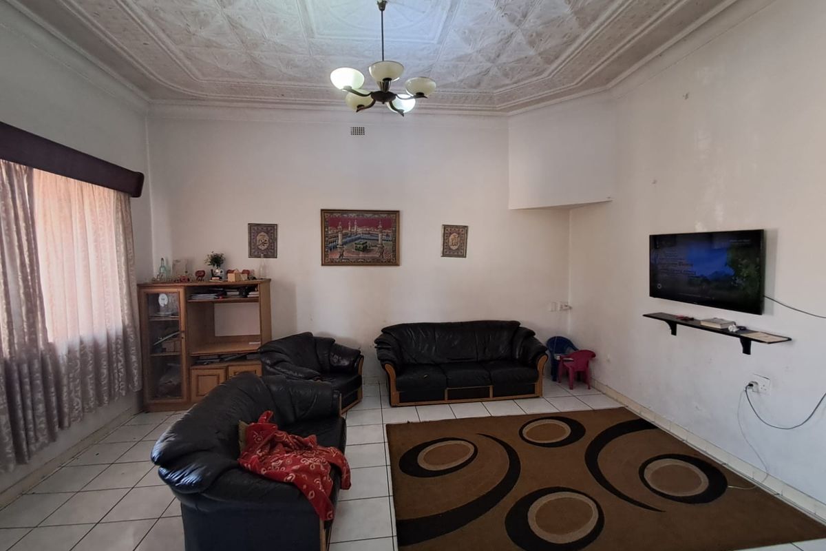 A living room featuring an ornate plaster ceiling and tiled flooring, offering a spacious layout with potential for cosmetic updates.