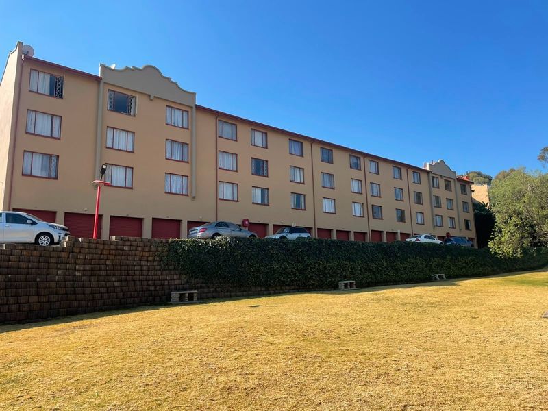 Exterior view of a multi-story apartment complex featuring a row of garage doors, a retaining wall, and a large front lawn area.