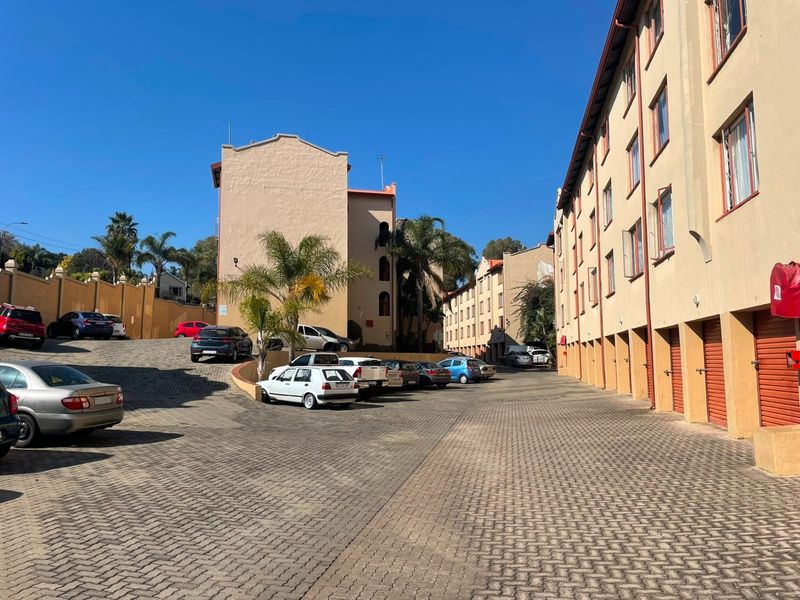 Exterior view of an apartment complex featuring a paved parking area, multiple garage units, and multi-story residential building facades.