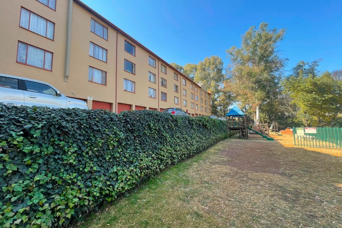 Exterior view of a multi-story apartment complex featuring integrated garage units, a landscaped hedge, and a communal playground area.