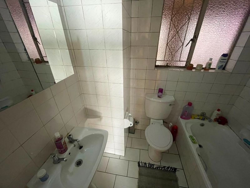 A compact bathroom featuring a pedestal basin, toilet, and bathtub with tiled finishes and an obscured glass window for privacy.