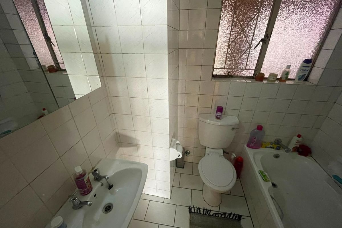 A compact bathroom featuring a pedestal basin, toilet, and bathtub with tiled finishes and an obscured glass window for privacy.