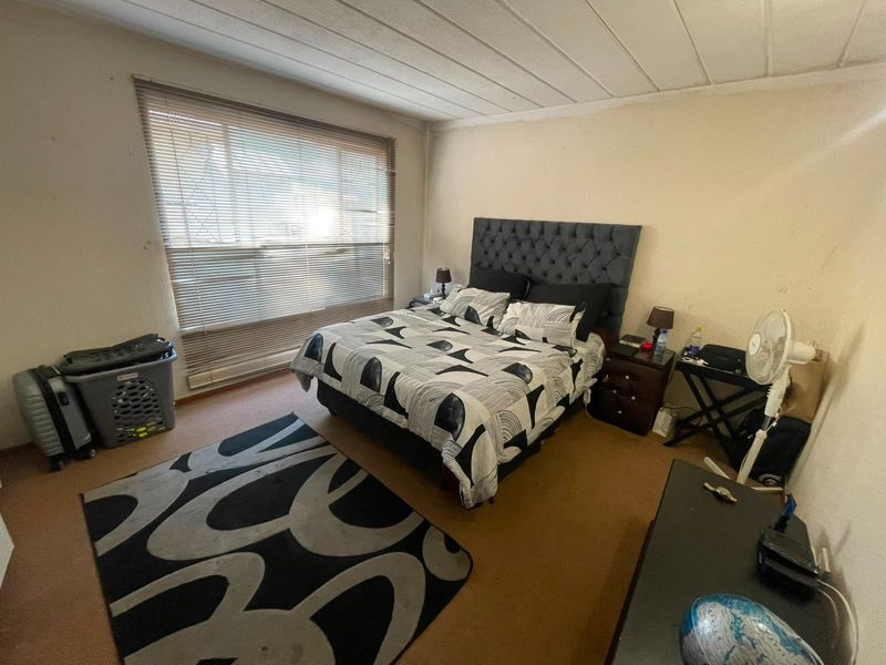 A bedroom featuring a textured ceiling and large window with venetian blinds. The space requires cosmetic updates to the wall finishes.