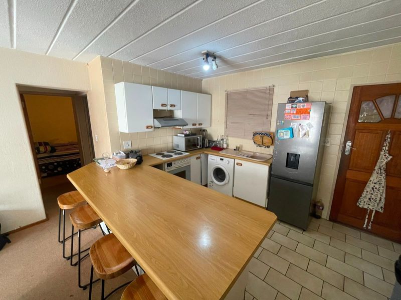 Functional kitchen featuring built-in cabinetry, electric hob, oven, extractor fan, and a breakfast bar, with tiled flooring and backsplash.