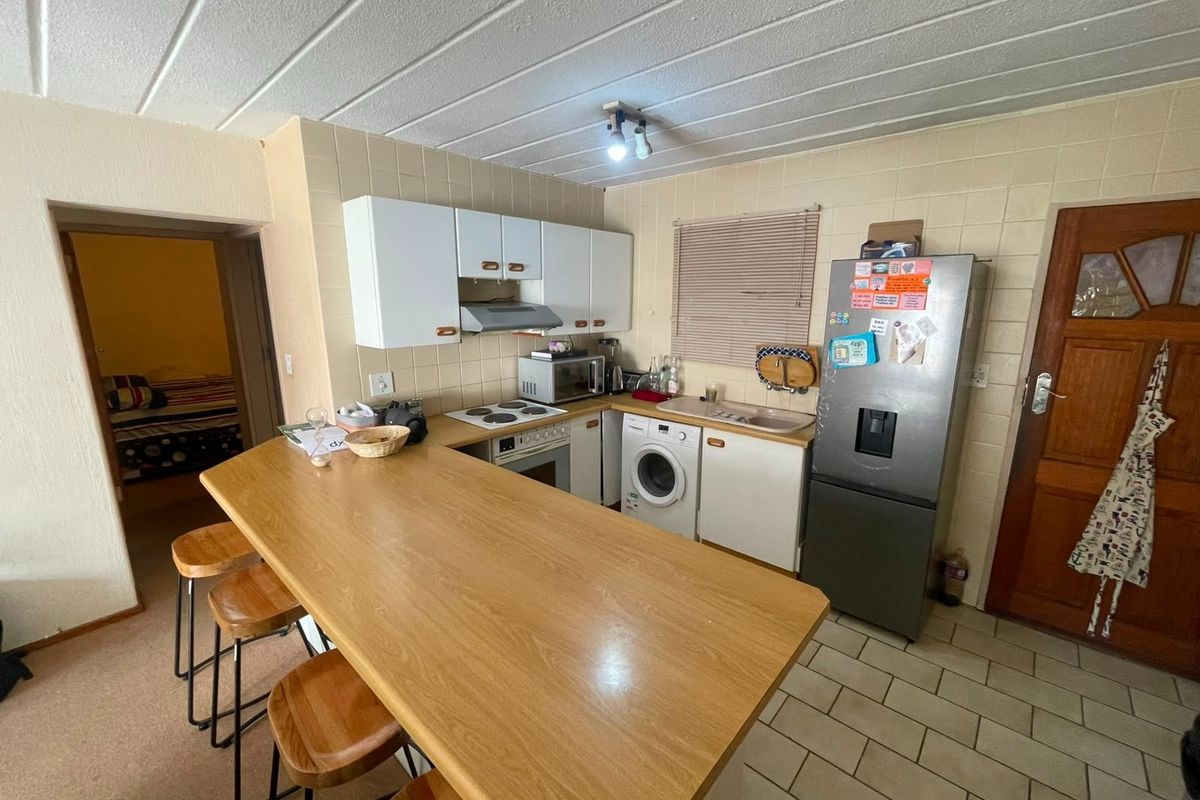 Functional kitchen featuring built-in cabinetry, electric hob, oven, extractor fan, and a breakfast bar, with tiled flooring and backsplash.