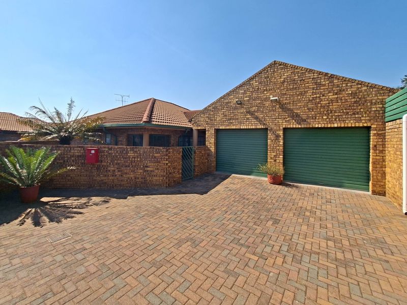 Front exterior view of a townhouse featuring a face brick facade, double garage with roll-up doors, and a paved driveway.