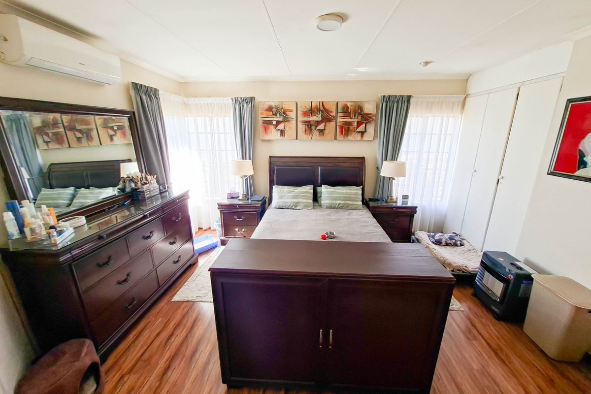 A well-proportioned bedroom featuring laminate flooring, built-in cupboards, and a wall-mounted split-system air conditioner for climate control.