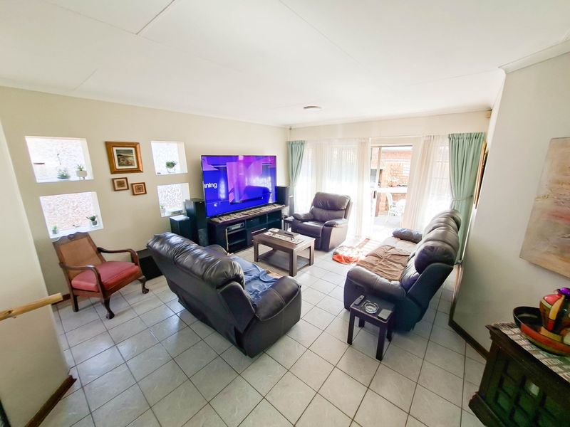 A spacious living room featuring tiled flooring, recessed lighting, and a sliding glass door providing access to the outdoor area.