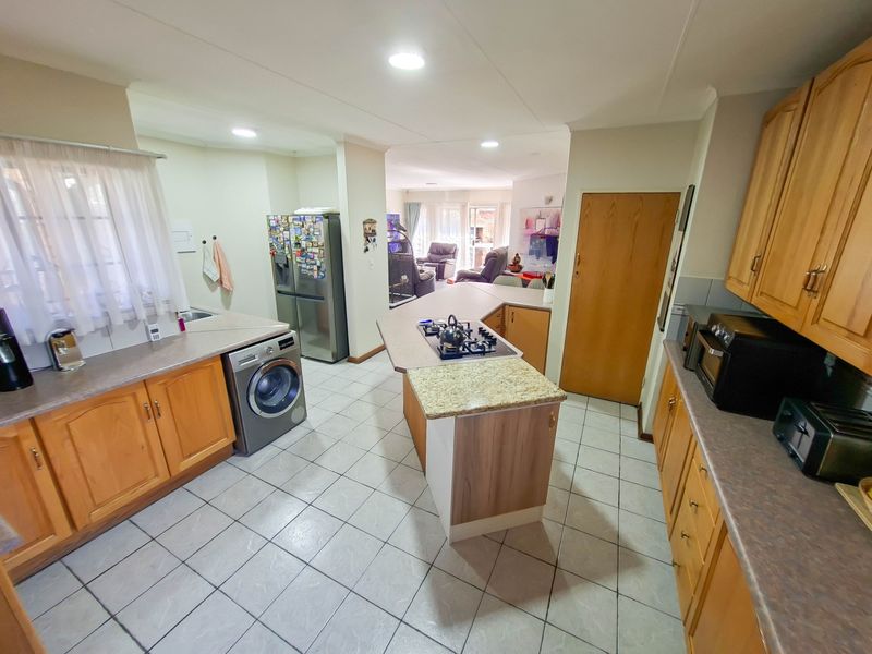 Open-plan kitchen featuring wooden cabinetry, laminate countertops, a central island with a gas hob, and tiled flooring, flowing into the adjacent living area.